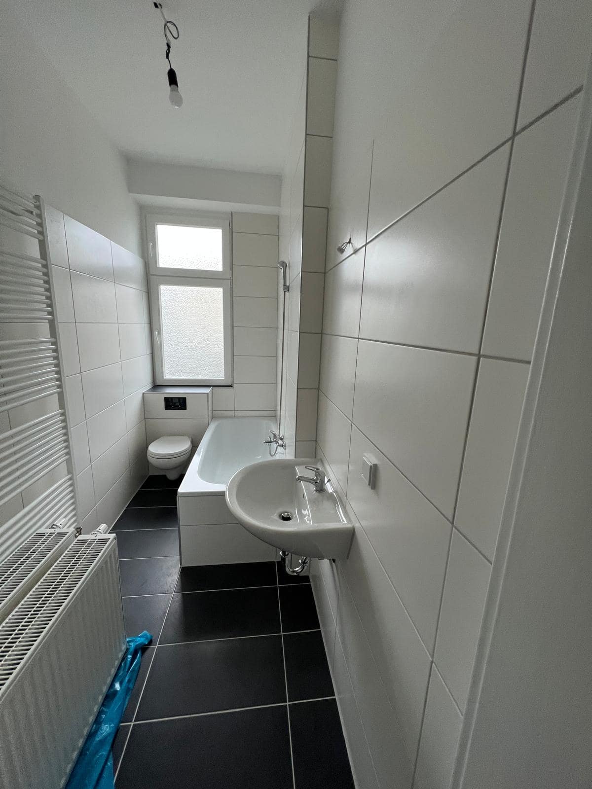 Frisch renoviertes Bad mit Wanne, Waschtisch und dunklen Bodenfliesen – Amiris Badsanierung